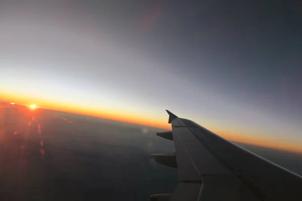 wing of airplane flying above window at sunset