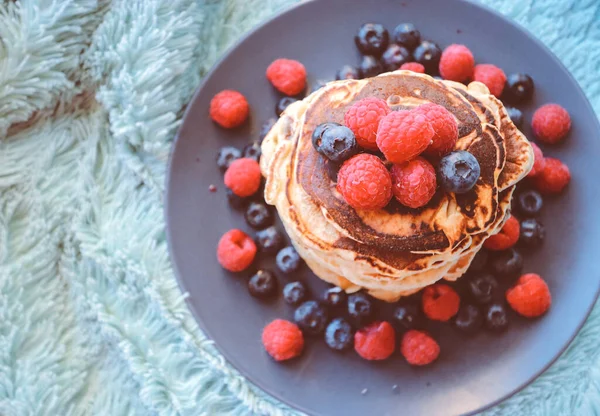 pancakes with raspberries and blueberries on a plate on a dark background.