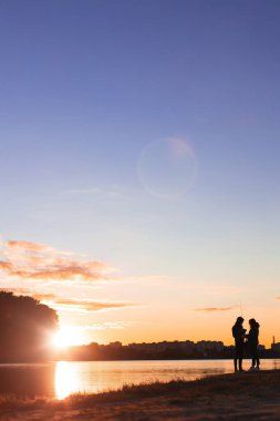 Romantik çiftin hafta sonu nehir kıyısında aktif bir balık tutma tarzı günbatımı manzaralı arka plan, odaksız siluet konsepti dikey fotoğrafçılık