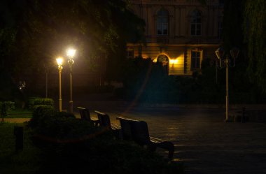 Gece sokağı eski şehir meydanı. Üniversite kampüsünde fener ışıkları, odaklanmamış fotoğraf konsepti, boş alan, ahşap bank.