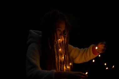 soft focus atmospheric night holiday concept photography of face woman with dreadlocks and garland in hands