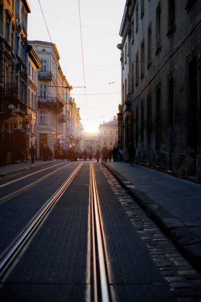 Günbatımında eski şehrin dramatik caddesi atmosferik ışıklandırma, dikey fotoğrafçılık perspektifi ön planda tramvay taşımacılığı altyapısı