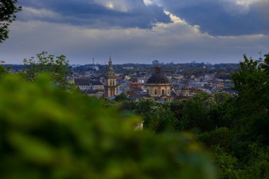 Güzel Lviv Ukrayna şehri panoramik manzaralı kilise ve belediye kulesi park alanından ön planda odaklanmamış yeşillik manzaralı dramatik bulutlu ışık