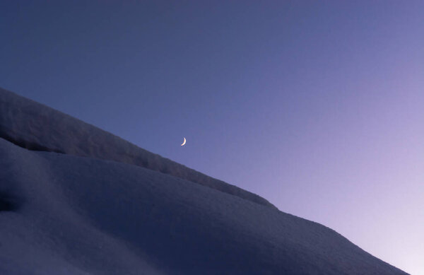 Moon over the roof covered with snow on a clear winter evening