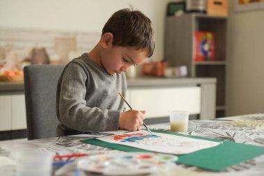 Beyaz çocuk evde zevkle resim yapıyor.