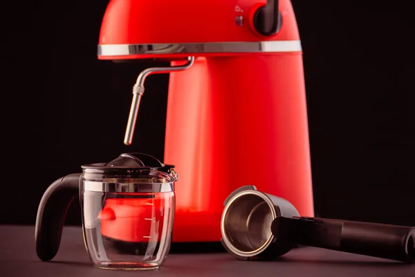 Siyah arka planda cam sürahi olan kırmızı bir kahve makinesi. Espresso yapmak için mutfak aletleriyle dolu sakin bir hayat..