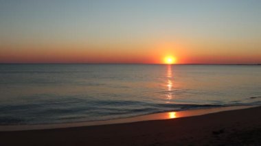 Kumlu sahilde, günbatımının okyanusa yansıttığı hafif dalgalar.