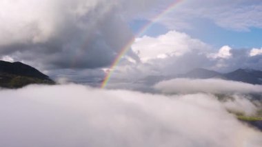 Puffy clouds forming as a bright, colourful double rainbow lights up the sky, with sea loch lake and green mountains in beautiful Scotland. 