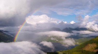 Puffy clouds forming as a bright, colourful double rainbow lights up the sky, with sea loch lake and green mountains in beautiful Scotland. 