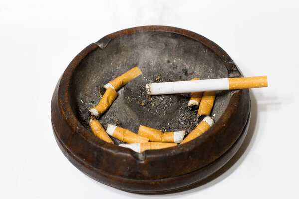 пепельница с погасшими сигаретами и зажженной сигаретой на белом фоне