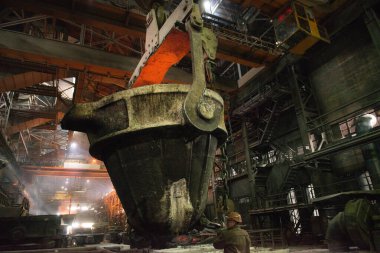 Çelik fabrikasındaki sıcak metalle tankların yanında çalışan çelik işçisi.