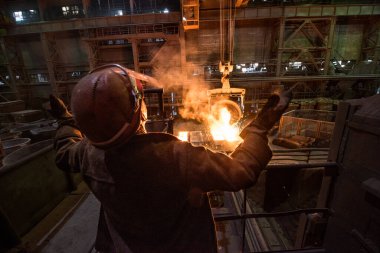 Çelik fabrikasındaki tanklardan sıvı metal dökerken çelik işçisi.