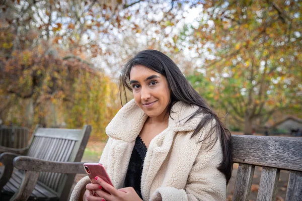 Girl Sitting Bench Park Uses Her Phone Smiles Attractive Indian — Stok fotoğraf
