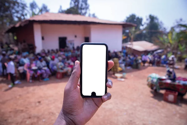 Makieta Ekranu Smartfona Trzymanego Rękę Afrykańską Wioską Tle Ludźmi Siedział — Zdjęcie stockowe