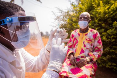 Afrikalı bir doktor yaşlı bir hastaya aşı enjekte etmek için bir şırınga hazırlıyor. Afrika 'da Covid-19' dan aşı kavramı