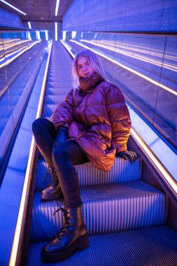 Metroda yürüyen merdivenlerde oturan genç bir kız, kışın beyaz bir genç.