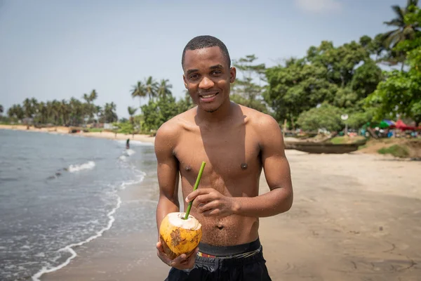 Young black smiling boy on beach vacation enjoying coco juice after bathing.