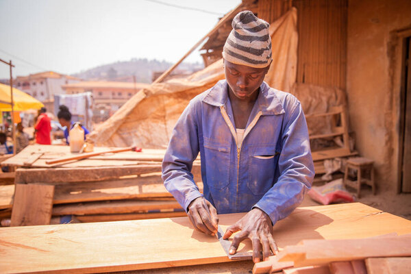 African carpenter takes measurements with a ruler and a pen on a wooden board