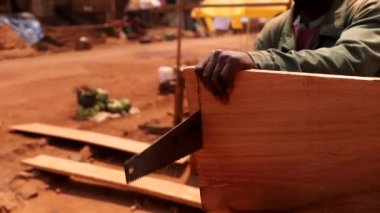 Afrikalı marangoz el testeresiyle bir tahta kesiyor, atölyede çalışıyor..