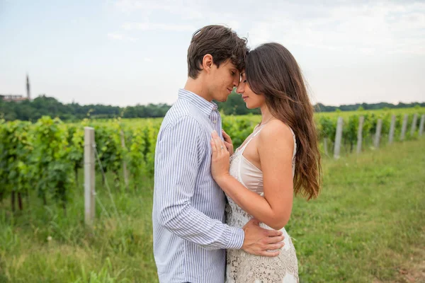 Young couple models huddle nose to nose in a vineyard in the countryside.