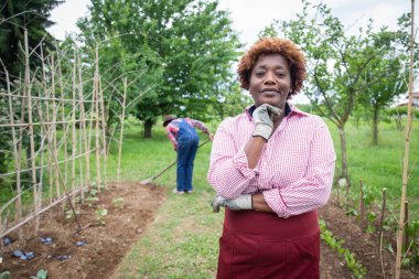 Portrait of a peasant woman in her cultivated field, her husband digs the earth, a small business entrepreneur.
