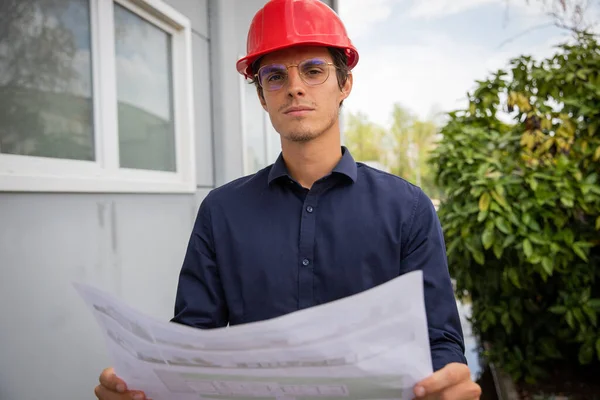 An engineer with a floor plan in hand wears a protective case on the construction site