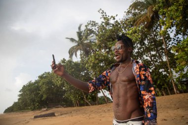 Young man vacationer looks at the sea and takes a selfie on the beach by the seaside.
