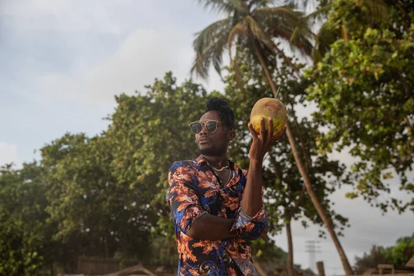 Frame of a young man looking into the distance and holding a large coconut with a straw.