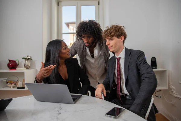 Colleagues discuss at work using a laptop, multi-ethnic business group