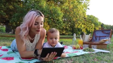 Anne, halka açık bir parkta piknik yaparken tablet kullanan bir çocuk olan oğlunu eğitiyor..