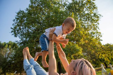Genç anne piknik sırasında onu havaya kaldırarak oğluyla oynar. Anneler Günü..