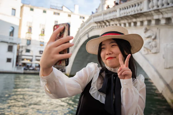 微笑的游客一边在威尼斯里阿尔托桥下做胜利的V标志 一边自拍 — 图库照片