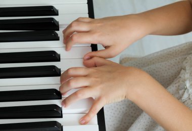 Sarışın küçük bir kız bebek oturma odasında dijital piyano çalıyor, arkadan yakın plan. Bir çocuk müzik aleti çalmayı öğrenir. Çocuklar için erken dönem müzik eğitimi.