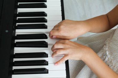 Sarışın küçük bir kız bebek oturma odasında dijital piyano çalıyor, arkadan yakın plan. Bir çocuk müzik aleti çalmayı öğrenir. Çocuklar için erken dönem müzik eğitimi.