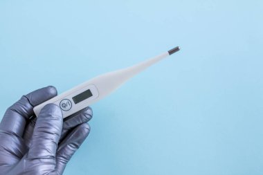 Gri tıbbi eldivenli bir el açık mavi arkaplanda bir termometre tutar, yazı için bir yer, üst görünüm