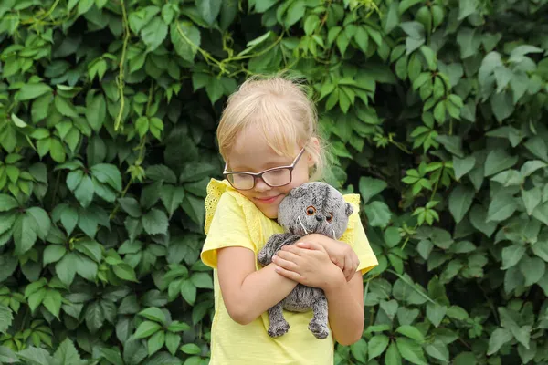 Linda niña abraza su juguete favorito gris gatito albahaca —  Fotos de Stock