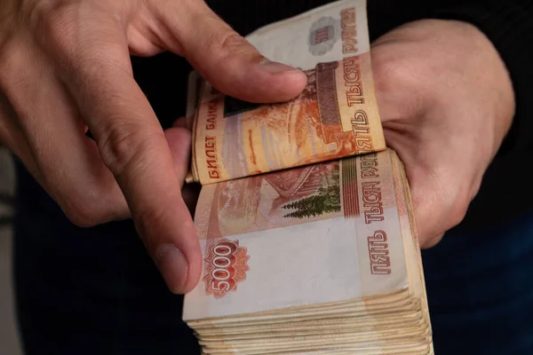 Τα χέρια ενός ανθρώπου σε κοντινό πλάνο θεωρεί ένα πακέτο των ρωσικών χρημάτων να είναι πέντε χιλιάδες χαρτονομίσματα. Εικόνα Αρχείου