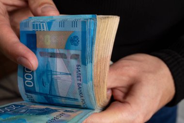 Yakın planda bir adamın elleri, Rus parasının iki bin dolar olduğunu düşünür..
