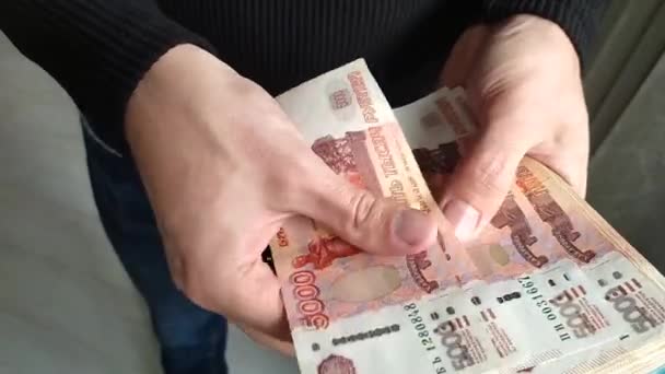 Een man heeft een hoop geld in zijn handen. Een close-up van een mensenhand telt een bundel rekeningen voor vijfduizend Russische roebel. — Stockvideo