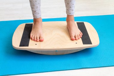 Çocuk ayak valginden ahşap dengeleyiciye egzersiz yapıyor. Childs 'ın bacakları yakın plan. Çocuklar için fizik tedavi dersleri