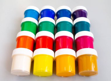 A set of closed jars with gouache of different colors are laid out in rows on a gray background. Hobby - drawing.