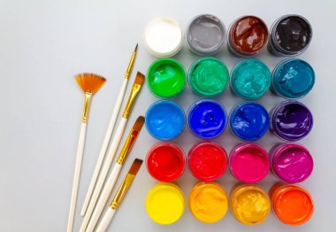 Gri arka planda farklı renkte gagalı ve fırçalı kavanozlar. Hobi - çizim. Üst görünüm