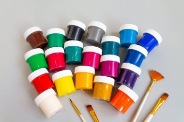 Farklı renklerde gouache ve gri arkaplan üzerine çizim için fırça içeren kapalı kavanozlar..