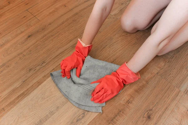 Girl washes the laminate floor with her hands in rubber gloves. House cleaning services.