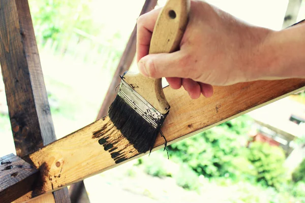 Closeup male hand with paintbrush in hand and painting natural wooden planks and beams. Selected focus.