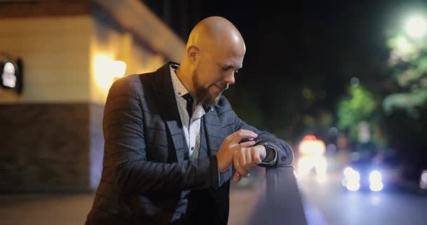Az üzletember okos órát használ az éjszakai városban. — Stock videók