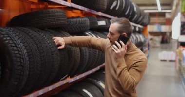 Adam akıllı telefonlara danışarak araba tamirhanesinde kış lastiklerini seçiyor.
