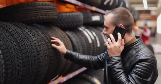 Man kiest winter autobanden in auto shop consulting door smartphone — Stockvideo