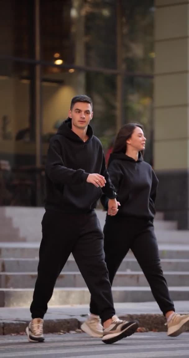 검은 옷을 입은 두 사람 이 도시의 수직 영상을 통해 길을 건넌다 — 비디오