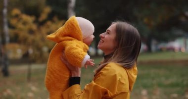 Mutlu anne fırlatır ve bebeğini sonbahar parkında yakalar.